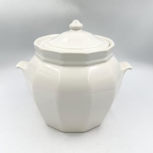 May include: A white ceramic lidded jar featuring an octagonal body with faceted sides and two small side handles. The lid has a matching octagonal shape and a central knob handle. The surface is smooth and glossy with a uniform white finish.
