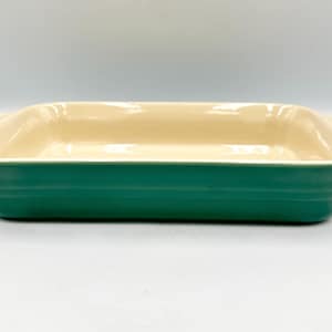 May include: Rectangular baking dish with a cream-colored interior and a teal exterior. The dish has a slightly flared rim and handles on each end. The exterior has horizontal ridges. A kitchenware item.