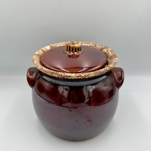 以下が含まれることがあります： ヴィンテージの濃い茶色のセラミック製のキャセロールで、お揃いの蓋が付いています。 蓋には、テクスチャ加工されたタン色の縁と小さな装飾的なハンドルが付いています。 キャセロールには両側に2つの小さなハンドルがあり、光沢のある仕上がりです。 クラシックなキッチン用品です。