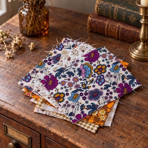 May include: A stack of square fabric swatches featuring various patterns including a vibrant floral print with purple, blue, and orange flowers on a white background, a solid orange floral print, and a light brown and white gingham check pattern.