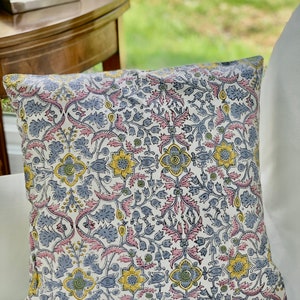 May include: A white pillow with a floral pattern in shades of pink, blue, yellow, and green. The pattern is a repeating design of flowers and leaves.