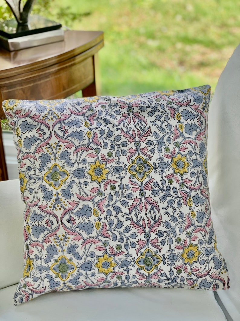 May include: A white pillow with a floral pattern in shades of pink, blue, yellow, and green. The pattern is a repeating design of flowers and leaves.