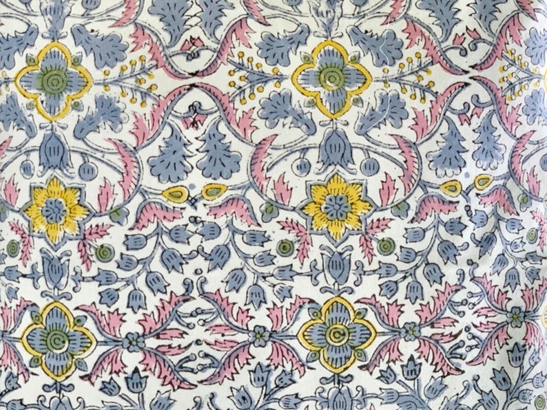 May include: A white fabric with a repeating floral pattern in shades of pink, blue, and yellow. The pattern features stylized flowers, leaves, and vines.