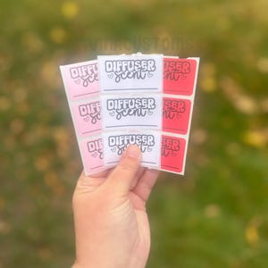 May include: Nine white labels with black text that reads "DIFFUSER scent" with a heart on either side of the word "scent". Three of the labels are pink and six are red.