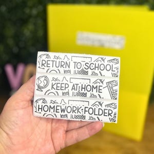 May include: Three rectangular white labels with black text and school-themed line art icons. The labels read RETURN TO SCHOOL, KEEP AT HOME, and HOMEWORK FOLDER in a bold, sans-serif font, surrounded by small illustrations of globes, rulers, and books.