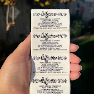 May include: A vertical strip of four white rectangular stickers with black text. Each sticker features the heading car diffuser care in a script font, followed by instructions to unscrew the wooden cap, remove the plastic stopper, and hang.