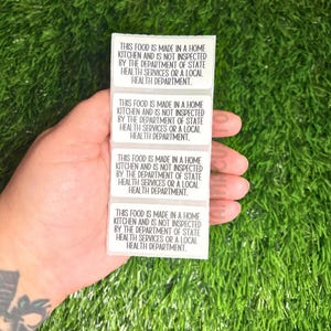May include: Four white rectangular stickers with black text that reads "This food is made in a home kitchen and is not inspected by the Department of State Health Services or a local Health Department."