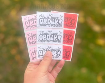 May include: A sheet of rectangular stickers featuring the text "love your ORDER? leave a review!" in a bold, stylized font with heart icons. The stickers are arranged in columns with alternating light pink, white, and red background colors.