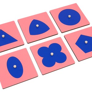 May include: Six pink square wooden tiles with blue shapes cut out. The shapes are a circle, triangle, oval, pentagon, flower, and a teardrop shape.