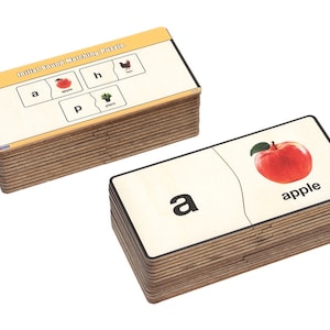 May include: A set of wooden puzzle pieces with images and letters. The pieces are stacked on top of each other. The image shows the letter "a" and a picture of an apple. The text "Initial Sound Matching Puzzle" is on the top piece.