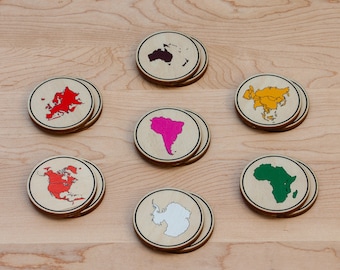 Puede incluir: Conjunto de siete posavasos de madera que representan los diferentes continentes del mundo. Cada posavasos es redondo y tiene un continente de color diferente delineado en negro. Los continentes son: América del Norte, América del Sur, Europa, Asia, África, Australia y la Antártida.