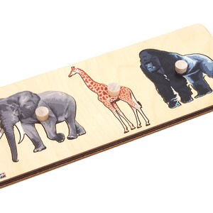 May include: Wooden puzzle with three animal shapes: an elephant, a giraffe, and a gorilla. Each animal is cut out and has a wooden knob for easy handling.