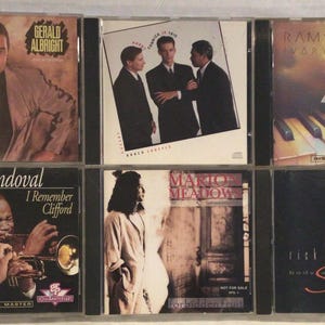 May include: A collection of six music CDs in plastic jewel cases. The covers feature various artists including Gerald Albright, Ramsey Lewis, and Arturo Sandoval, with titles like I Remember Clifford, Ivory Pyramid, and Body and Soul displayed.
