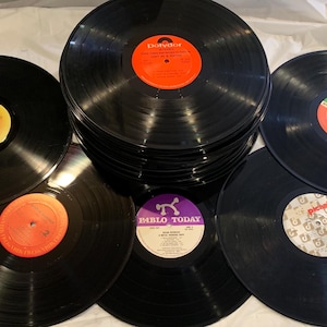 May include: A collection of black vinyl records with colorful labels. Some records are stacked, while others are spread out, showcasing various album art and designs. The labels feature shades of orange, yellow, green, and purple.