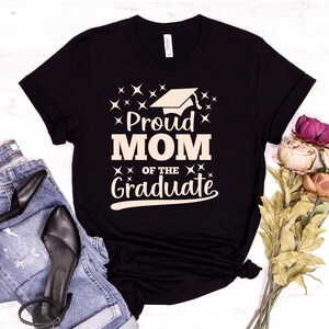 May include: Black t-shirt with a white graphic that says "Proud Mom of the Graduate" with a graduation cap icon.