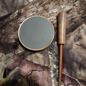 May include: A round, gray, wooden target with a gold rim and a wooden dowel with red, green, and white stripes.