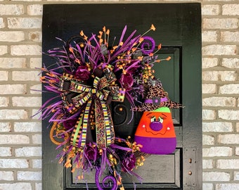 May include: A Halloween wreath with purple, orange, and green accents. A witch's hat with a candy corn face is attached to the wreath.