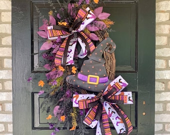 May include: A purple, green, and black Halloween wreath with a witch's hat, bows, and a variety of patterned ribbons. The wreath is decorated with fall foliage and berries.
