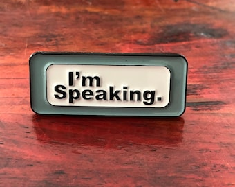 May include: A blue and black enamel pin with the text "I'm Speaking." in white letters.