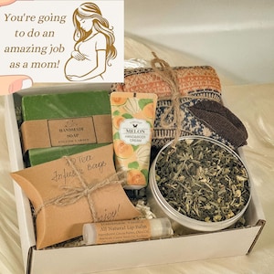 May include: A gift box filled with self-care items, including a green bar of soap, a tube of hand and body cream, a small tin of loose leaf tea, a brown paper bag with the words "12 Tea Infusir Bags" written on it, a brown and orange knitted scarf, and a lip balm tube with the words "Handmade Vanilla All Natural Lip Balm" written on it.