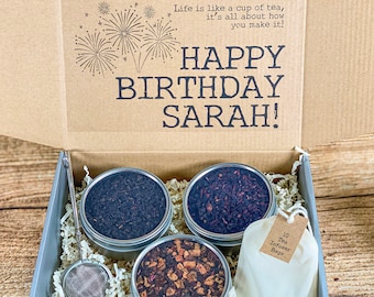 May include: A gift box with a brown lid and a grey base. The lid has a message that says "Life is like a cup of tea, it's all about how you make it!" and "HAPPY BIRTHDAY SARAH!" The box contains four small round containers of tea, a tea infuser, and a bag of 10 tea infuser bags.