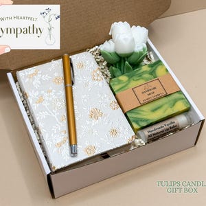 May include: A gift box containing a floral-patterned journal, gold pen, handmade soap, lip balm, and tulip-shaped candle. The box includes a card that reads "With Heartfelt Sympathy". The text "TULIPS CANDLE GIFT BOX" is also visible.