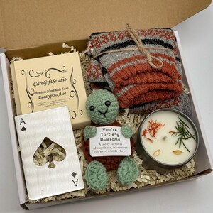 May include: A gift box containing a bar of soap, a metal Ace of Spades card, a crocheted turtle, a candle, and a pair of socks. The soap is labeled "CareGiftStudio Eucalyptus Aloe." The turtle has a tag that reads "You're Turtle-y Awesome."