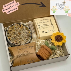 May include: A gift box containing a tin of dried herbs, a bar of soap, lip balm, a crocheted sunflower, a crocheted pot with a plant, and a package of tea bags. The box includes a card that says "Sending Hugs".