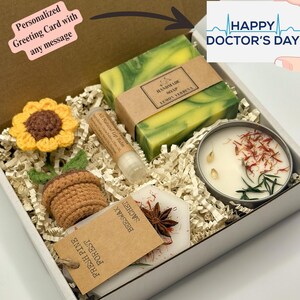 May include: A white gift box filled with a variety of items, including a crocheted sunflower, a small potted plant, a lip balm, a candle, a soap bar, and a wax sachet. The box is decorated with a personalized greeting card that says "Personalized Greeting Card with any message".