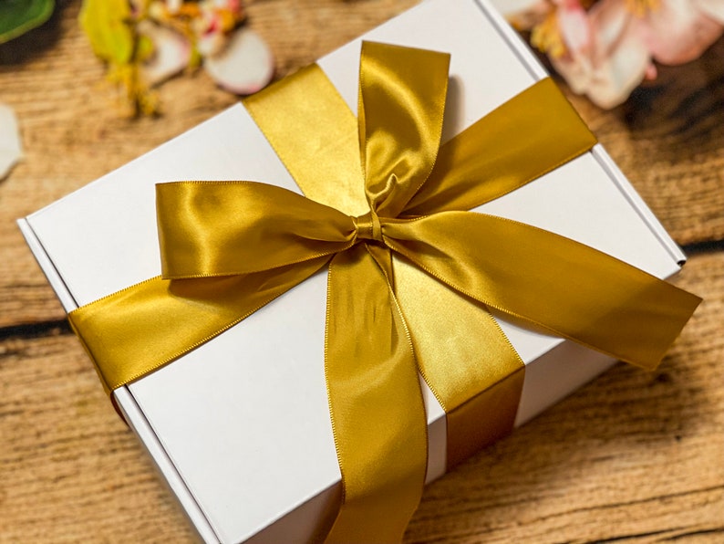 May include: A white gift box with a large gold satin ribbon tied in a bow.