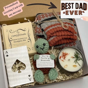 May include: A gift box containing a handmade soap, a crocheted turtle holding a sign, a candle, a deck of cards, and a pair of socks. The sign reads "You're Turtle-y Awesome". The box also includes a card that says "Best Dad Ever".