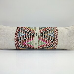 May include: A white rectangular cushion with a colourful geometric pattern on the front. The pattern is made up of triangles, squares, and diamonds in shades of red, blue, green, yellow, and black.