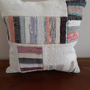 May include: A white throw pillow with a patchwork design featuring various colors and textures. The pillow is made of woven fabric and has a square shape.