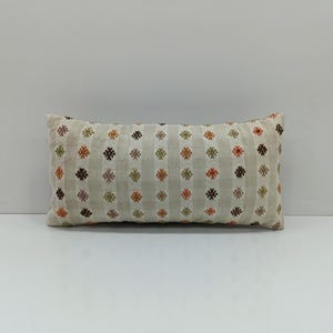 May include: A white rectangular pillow with a geometric pattern of small brown, orange, and green flowers. The pillow is made of a soft, woven fabric.