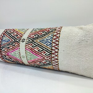 May include: A white lumbar pillow with a colourful geometric pattern woven into the fabric. The pattern is a mix of red, blue, green, yellow, and black.