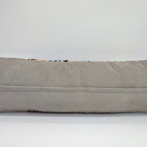 May include: A long, rectangular cushion with a beige velvet cover. The cushion has a zipper closure on the back.