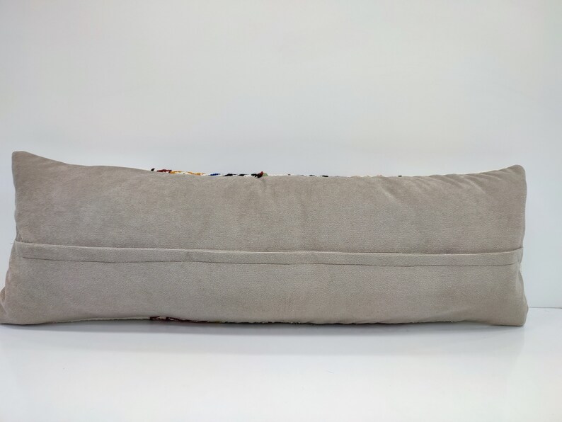 May include: A long, rectangular cushion with a beige velvet cover. The cushion has a zipper closure on the back.