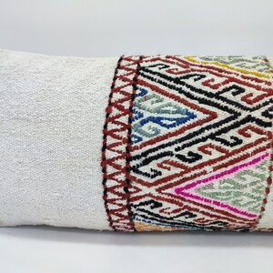 May include: White pillow with a colourful geometric pattern on one end. The pattern is made up of red, black, blue, green, and yellow threads.