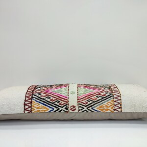 May include: A long, rectangular white cushion with a colourful geometric pattern woven into the centre. The cushion has a beige backing.