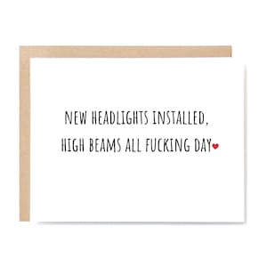 May include: A white greeting card with a brown border. The card has black text that reads "NEW HEADLIGHTS INSTALLED, HIGH BEAMS ALL FUCKING DAY" with a small red heart at the end.