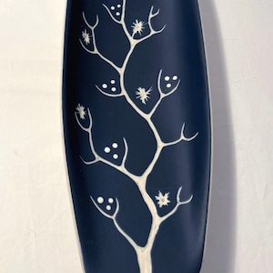 May include: A navy blue, oval-shaped decorative tray with a white tree branch design. The branches have small, round dots and star-like shapes. The tray is a decorative item for the home.