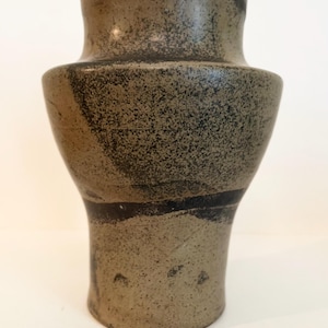 Könnte beinhalten: Eine Keramikvase mit breiter, abgerundeter Schulter und engem Hals. Die Oberfläche zeigt eine gesprenkelte, erdfarbene beige-graue Grundfarbe mit dunklen, anthrazitfarbenen abstrakten Pinselstrichen und einer durchgehend texturierten, matten Optik.