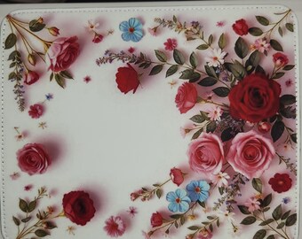 May include: White floral mousepad featuring a design of red and pink roses, blue and white accent flowers, and green leaves. The floral arrangement is set against a white background, creating a decorative and elegant look.