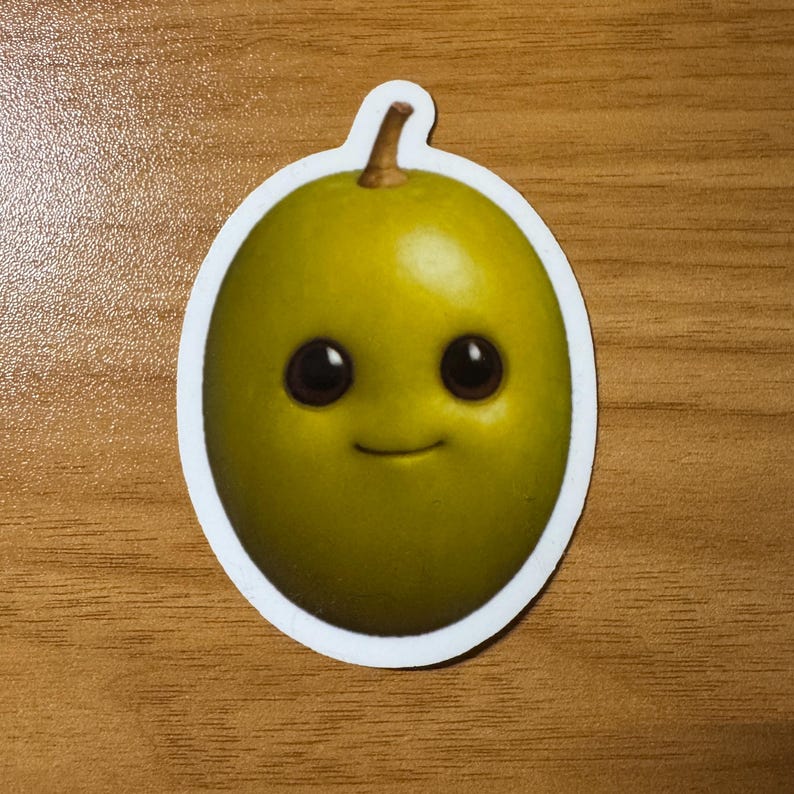 Puede incluir: Una pegatina con una aceituna de dibujos animados sonriente, con grandes ojos negros y una boca peque&ntilde;a y curvada. La aceituna es de color verde vibrante, con un peque&ntilde;o tallo marr&oacute;n. La pegatina tiene un borde blanco.