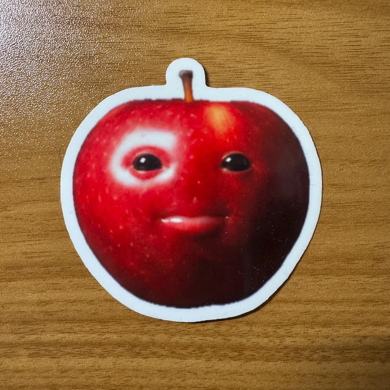 Puede incluir: Una pegatina de una manzana roja con una cara sonriente. La pegatina tiene un borde blanco y un peque&ntilde;o tallo en la parte superior. La cara de la manzana tiene dos ojos negros y una boca peque&ntilde;a y curvada.