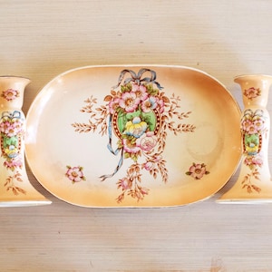 May include: A set of three vintage porcelain pieces with floral designs. The set includes a decorative tray and two matching candle holders.