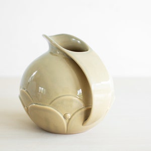 May include: A light green ceramic pitcher with a rounded body and a curved handle. The pitcher has a decorative design of raised circles and semi-circles.