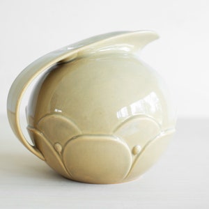 May include: A light green ceramic pitcher with a rounded body and a curved handle. The pitcher has a decorative design of raised circles and scalloped edges.