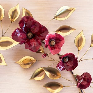 May include: A wall sculpture featuring a stylized branch with gold leaves and red flowers. The flowers are made of metal and have a textured surface.