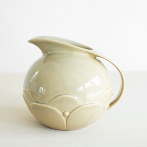 May include: A light green ceramic pitcher with a rounded body and a curved handle. The pitcher has a textured surface with a floral design.